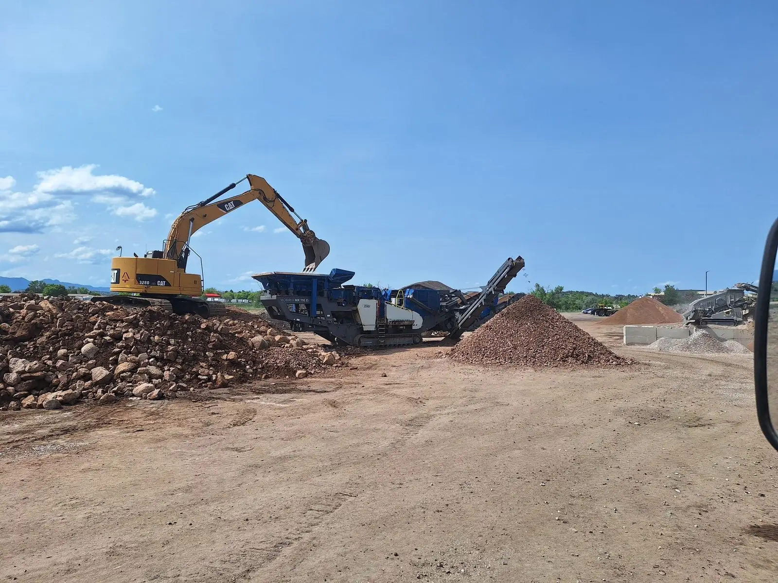 Cat excavator feeding a crusher unit with stockpiled product behind