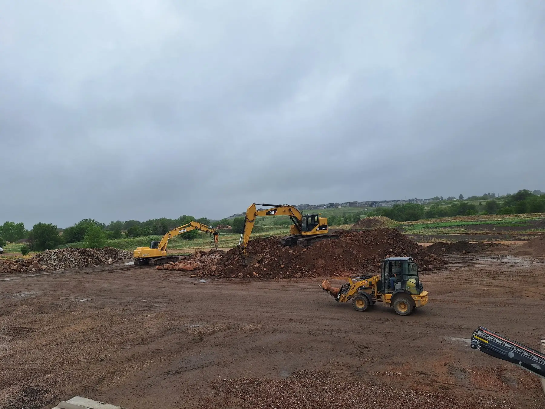 CrushRite yard with two excavators and a wheel loader working a red-stone stockpile