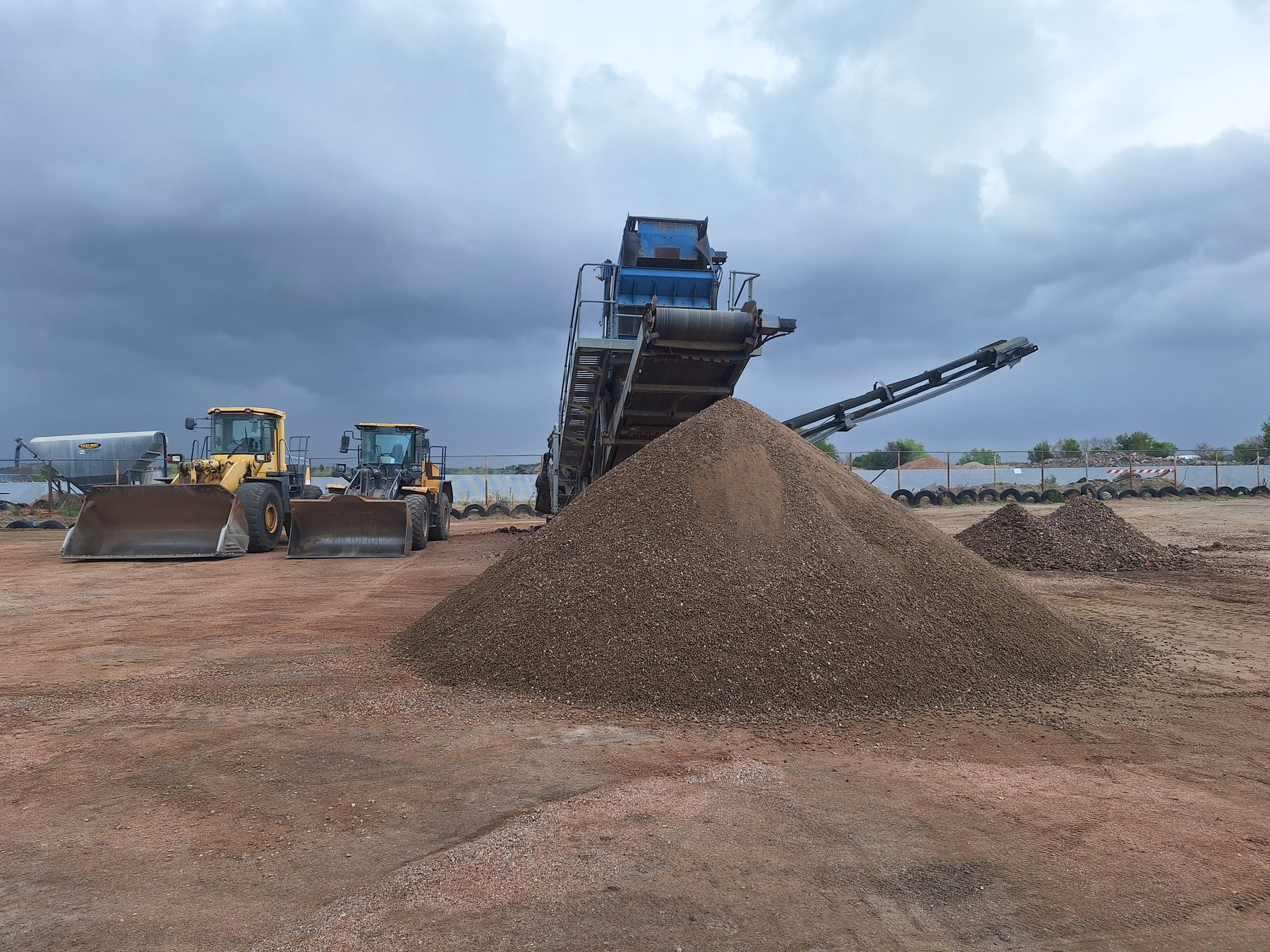 Two wheel loaders staged next to the screen plant with stockpiles under dramatic Colorado sky